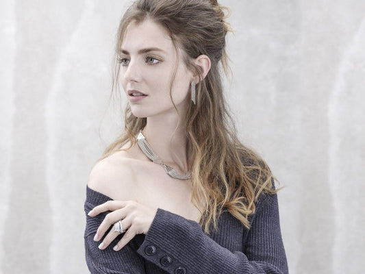 Mulher usando brincos curtos femininos em prata Carmo Joalheiros conjunto com colar e anéis para look elegante