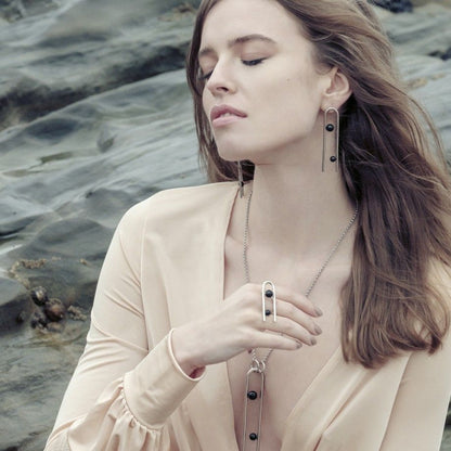 Mulher com conjunto Topazio 1874 mostrando anel clip feminino em prata com pedras negras e brinco longo