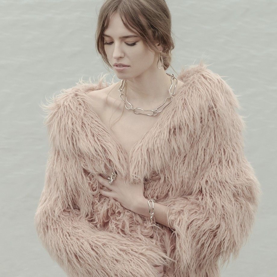 Modelo com casaco peludo rosa usando brincos femininos modernos e colar e pulseira de corrente da Carmo Joalheiros