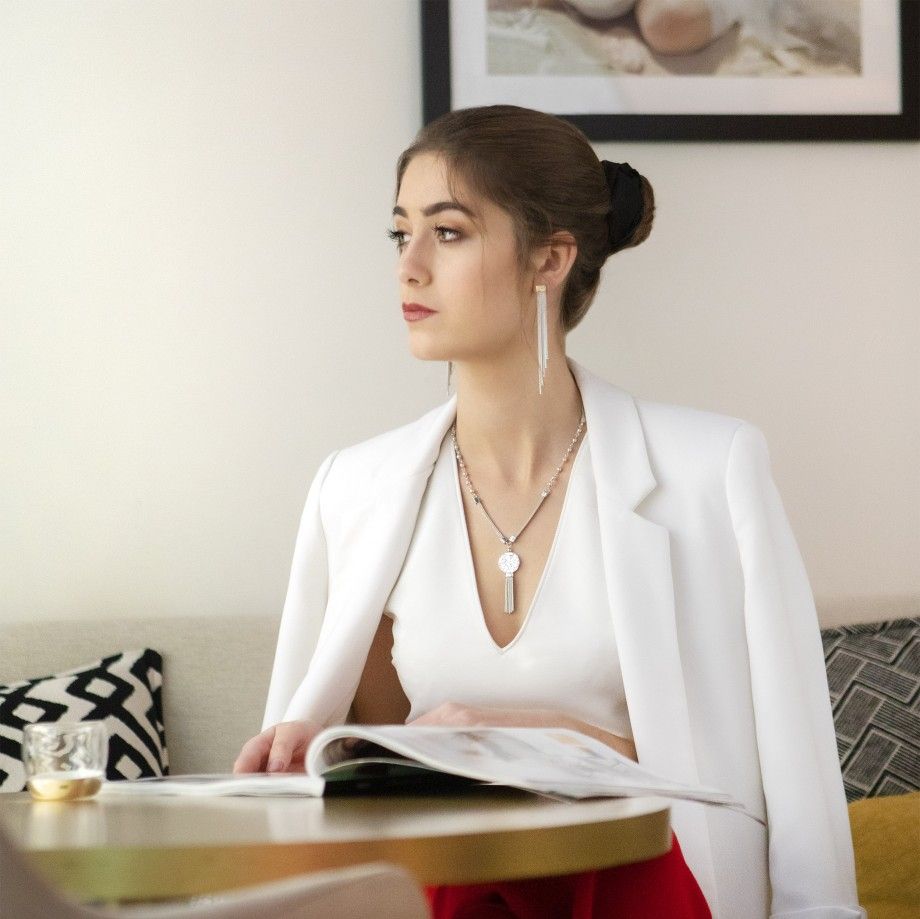 Mulher sentada com blazer branco mostrando colar círculo feminino da Carmo Joalheiros e brincos longos