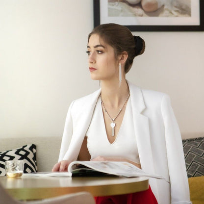 Mulher sentada com blazer branco mostrando colar círculo feminino da Carmo Joalheiros e brincos longos