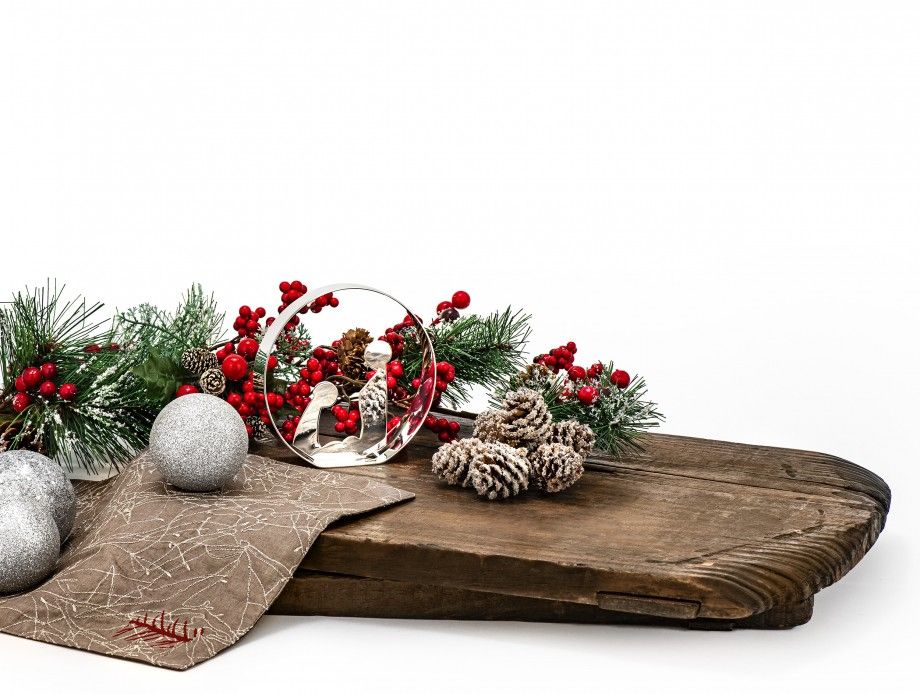 presépio Nazaré decorativo em vidro junto a pinhas, bolas prateadas e raminhos natalícios sobre tábua rústica