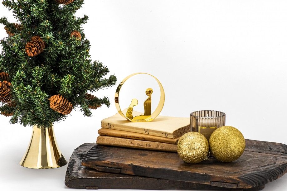 presépio decorativo dourado minimalista em metal sobre livros junto a árvore de Natal com bolas douradas