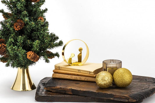 presépio decorativo dourado minimalista em metal sobre livros junto a árvore de Natal com bolas douradas