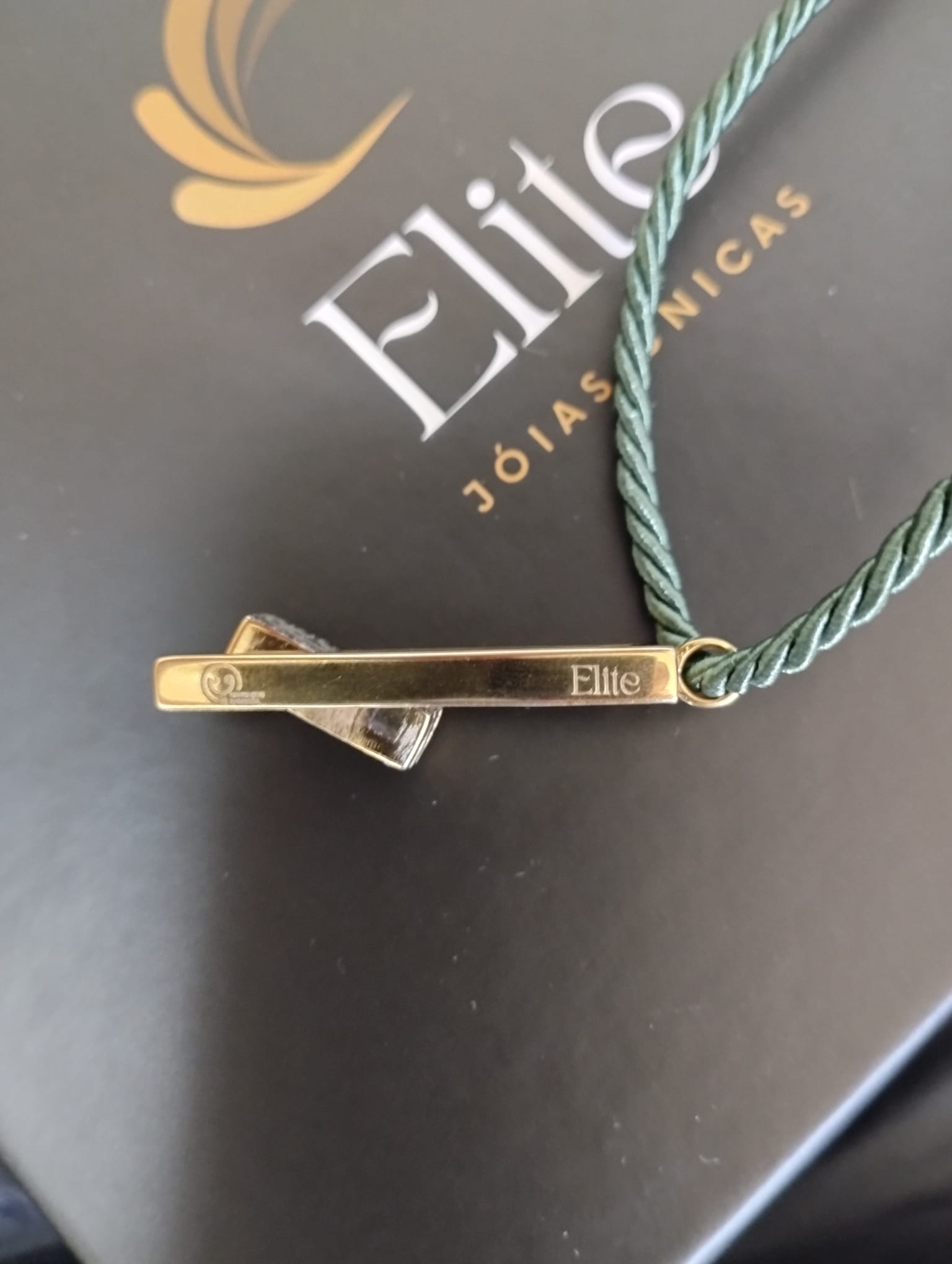 colar dos sorrisos exclusivo pingente barra dourada gravada Elite com cordao verde torcido sobre caixa preta